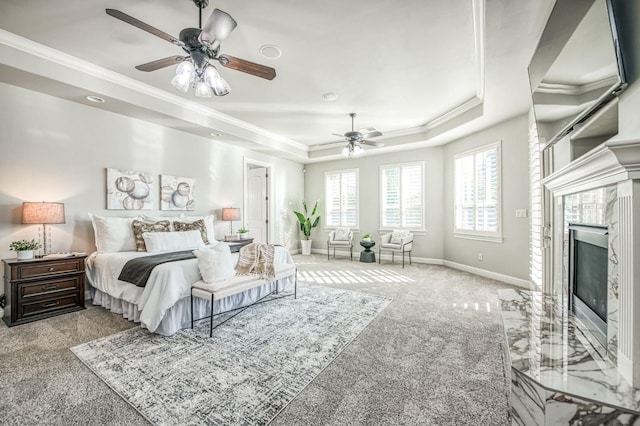 bedroom featuring ceiling fan, light colored carpet, a tray ceiling, and a fireplace