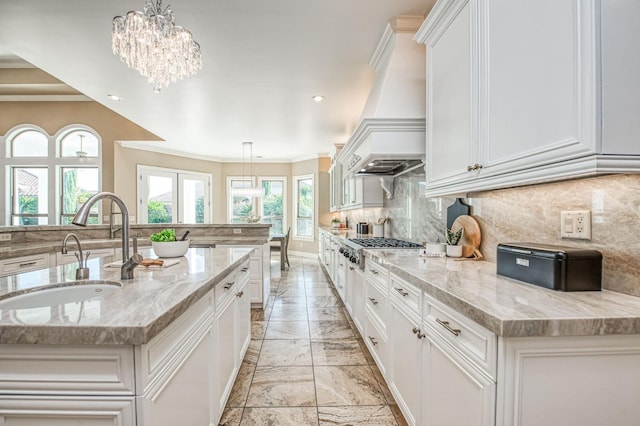 kitchen with decorative light fixtures, sink, light stone counters, and a kitchen island with sink