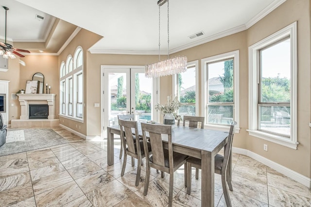 dining space with french doors, a fireplace, ceiling fan with notable chandelier, and ornamental molding