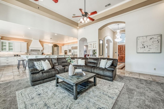 carpeted living room with ceiling fan with notable chandelier, a high ceiling, and crown molding