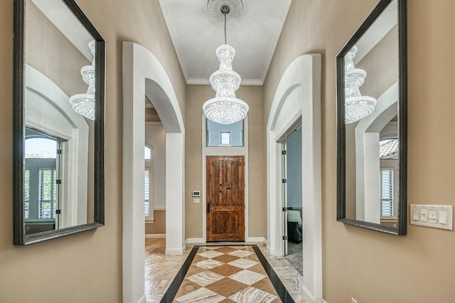 foyer entrance featuring plenty of natural light, crown molding, and a notable chandelier