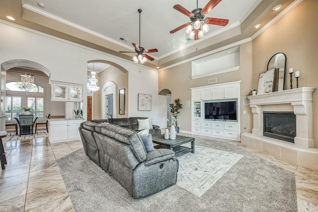 living room featuring ceiling fan, ornamental molding, a high ceiling, and a tile fireplace