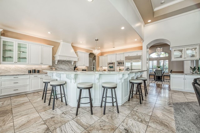 kitchen with white cabinetry, a large island with sink, custom range hood, and built in appliances