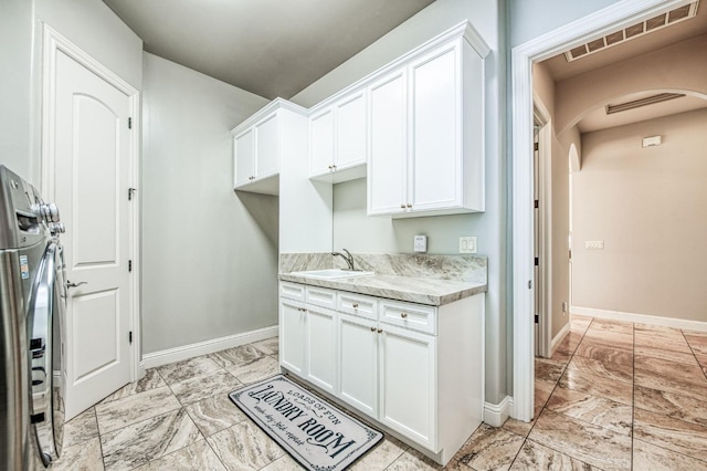 kitchen featuring sink, light stone counters, and white cabinetry