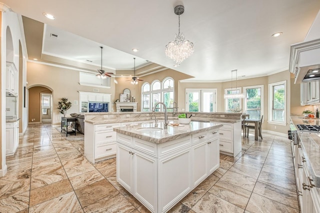 kitchen with decorative light fixtures, a kitchen island with sink, sink, and a raised ceiling