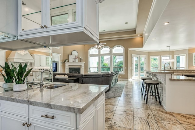 kitchen with a spacious island, white cabinetry, ceiling fan, sink, and light stone counters