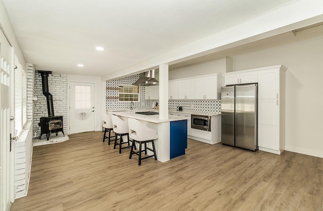 kitchen featuring wall chimney exhaust hood, a kitchen island, a kitchen bar, white cabinetry, and stainless steel appliances