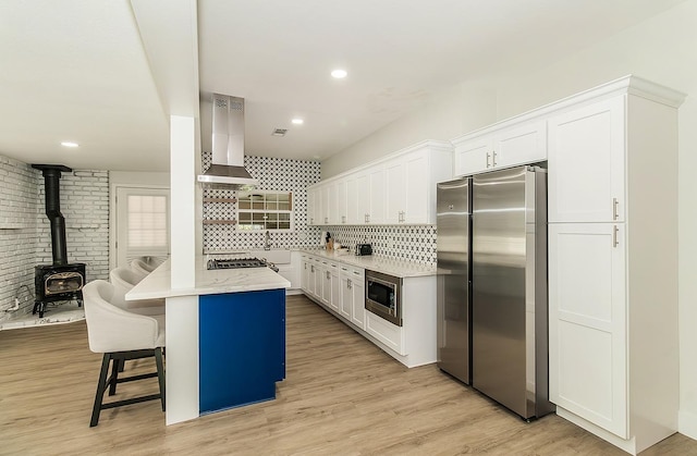 kitchen with wall chimney exhaust hood, white cabinetry, stainless steel appliances, tasteful backsplash, and a kitchen breakfast bar