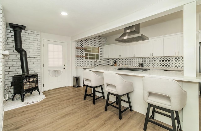 kitchen featuring wall chimney range hood, white cabinets, light hardwood / wood-style flooring, and a breakfast bar area