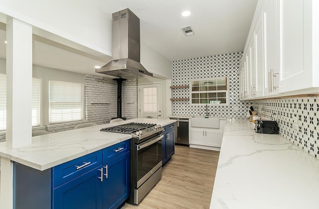 kitchen with island range hood, stainless steel appliances, light stone countertops, white cabinets, and sink