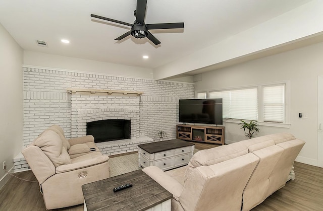 living room featuring ceiling fan, dark wood-type flooring, brick wall, and a brick fireplace