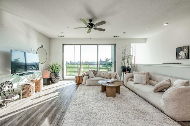 living area featuring visible vents, a textured ceiling, a ceiling fan, and wood finished floors