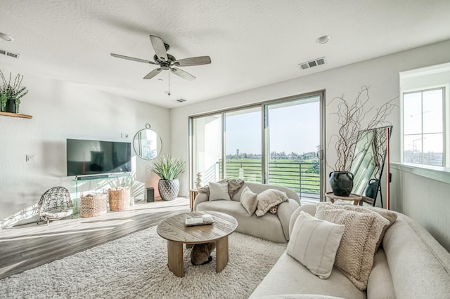 living room featuring a ceiling fan, visible vents, a textured ceiling, and wood finished floors