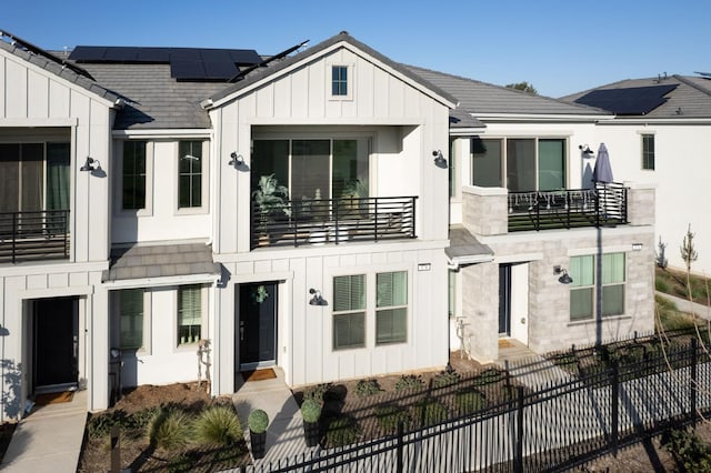 view of front of property featuring solar panels, a shingled roof, board and batten siding, a balcony, and fence private yard