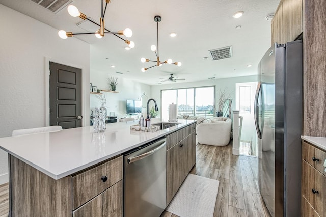 kitchen with light wood finished floors, visible vents, open floor plan, stainless steel appliances, and a sink