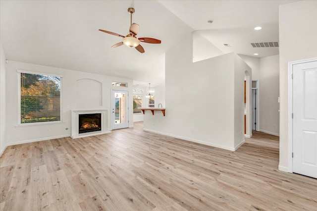 unfurnished living room featuring ceiling fan with notable chandelier, high vaulted ceiling, and light wood-type flooring