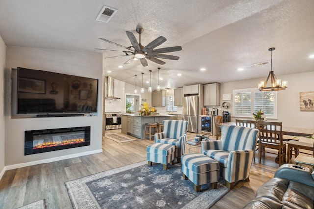 living room with wine cooler, vaulted ceiling, a textured ceiling, light wood-type flooring, and ceiling fan