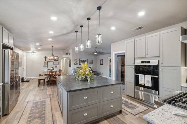 kitchen with gray cabinets, a kitchen island, appliances with stainless steel finishes, decorative light fixtures, and dark stone counters