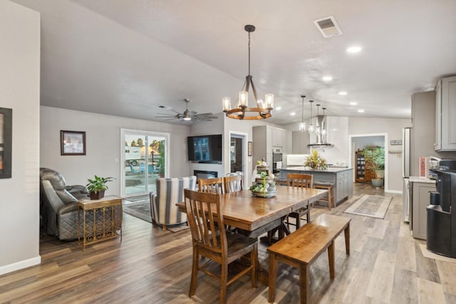 dining room with ceiling fan with notable chandelier, vaulted ceiling, and light hardwood / wood-style floors