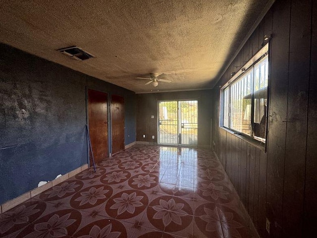 empty room featuring ceiling fan, wood walls, and a textured ceiling