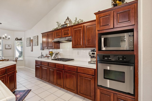 kitchen with tile countertops, stainless steel appliances, tasteful backsplash, light tile patterned flooring, and vaulted ceiling