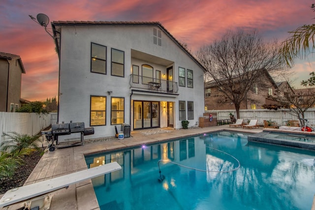 back house at dusk featuring a swimming pool with hot tub, a balcony, and a patio