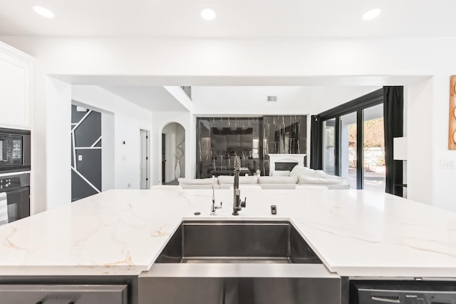 kitchen with light stone countertops, sink, white cabinets, and black appliances