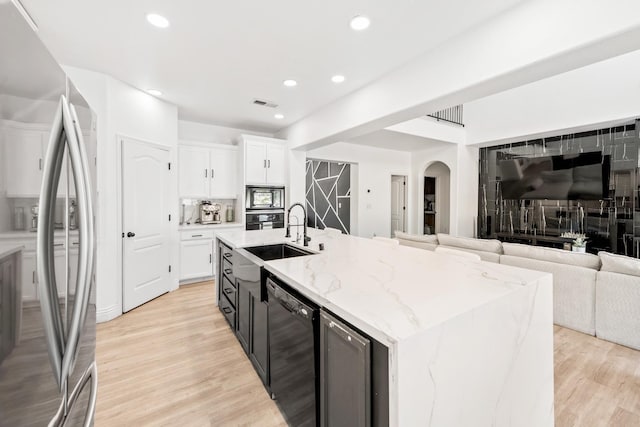 kitchen featuring white cabinets, black appliances, light hardwood / wood-style floors, a kitchen island with sink, and light stone counters