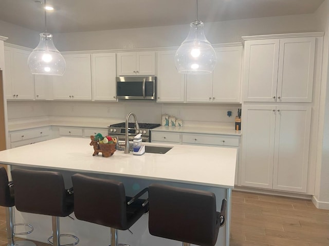 kitchen with decorative light fixtures, white cabinets, a center island with sink, and stainless steel appliances