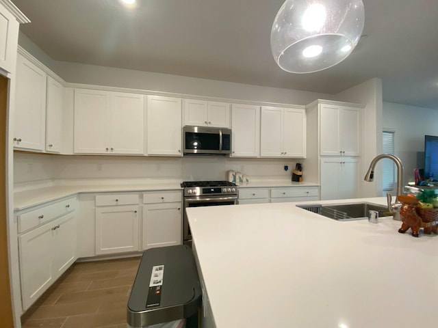 kitchen with stainless steel appliances, white cabinetry, hanging light fixtures, and sink