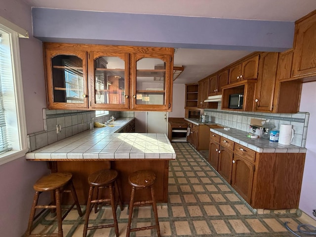 kitchen with tile counters, decorative backsplash, kitchen peninsula, and sink