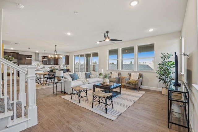 living room featuring ceiling fan with notable chandelier and light hardwood / wood-style flooring