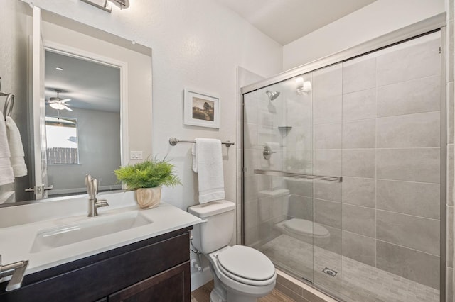 bathroom featuring toilet, vanity, ceiling fan, and an enclosed shower