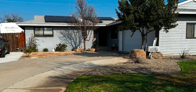 view of front of home with concrete driveway, fence, an attached garage, and solar panels