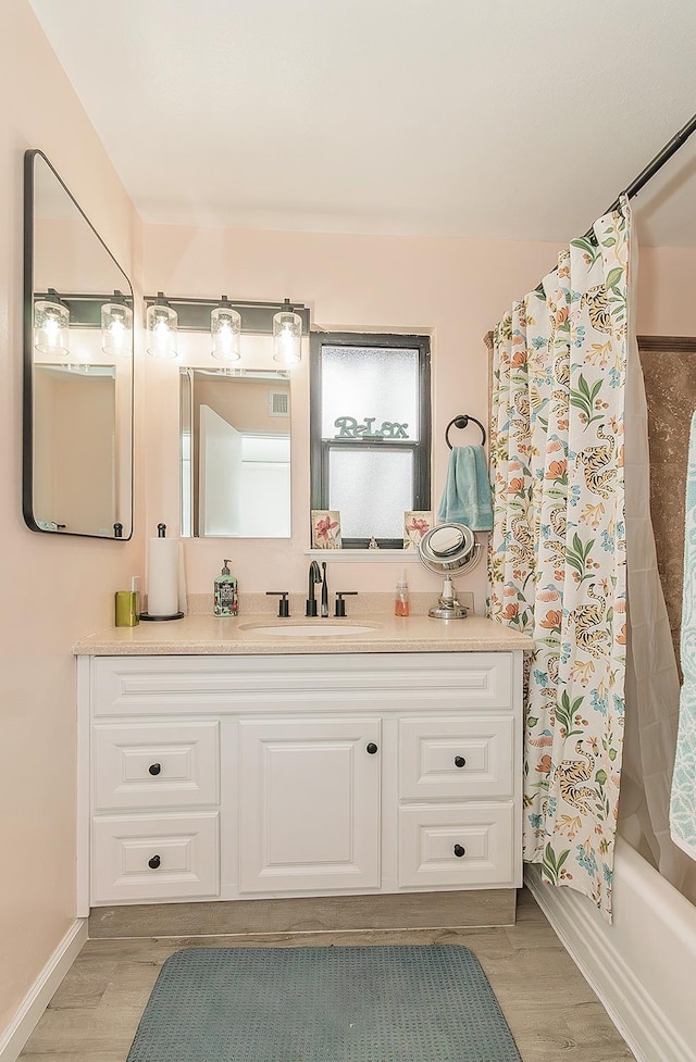 bathroom featuring shower / bathtub combination with curtain, baseboards, wood finished floors, and vanity