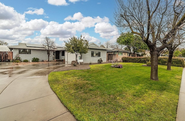 ranch-style home featuring driveway, roof mounted solar panels, and a front lawn