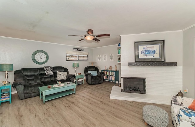 living room with a ceiling fan, a brick fireplace, crown molding, and wood finished floors