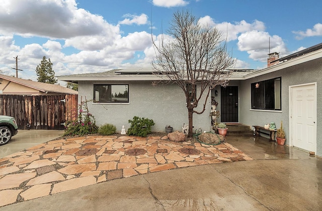 view of front of home with a patio, fence, solar panels, and stucco siding