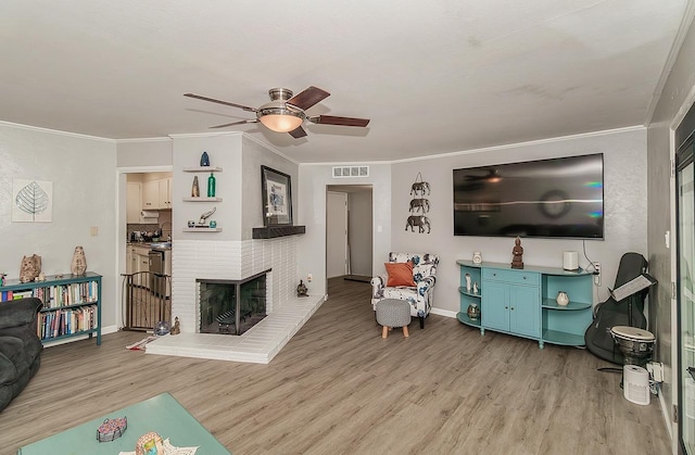 living area with light wood finished floors, visible vents, a ceiling fan, ornamental molding, and a fireplace