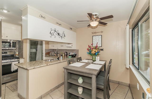 kitchen with stainless steel appliances, a peninsula, a sink, white cabinetry, and tasteful backsplash