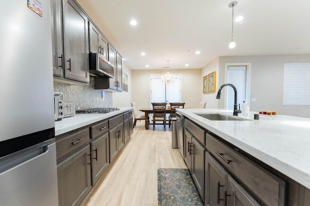 kitchen with light stone countertops, exhaust hood, decorative light fixtures, stainless steel appliances, and sink