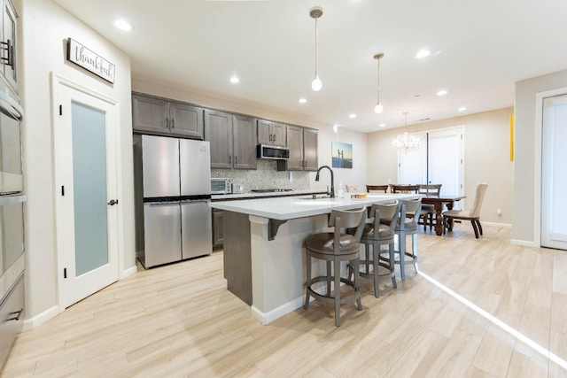 kitchen with light hardwood / wood-style floors, stainless steel appliances, a kitchen island with sink, pendant lighting, and sink