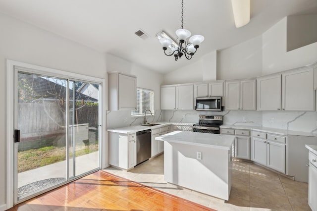 kitchen featuring a kitchen island, decorative light fixtures, stainless steel appliances, tasteful backsplash, and vaulted ceiling