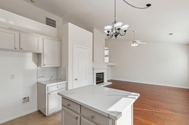 kitchen with a center island, lofted ceiling, decorative light fixtures, ceiling fan, and light stone counters