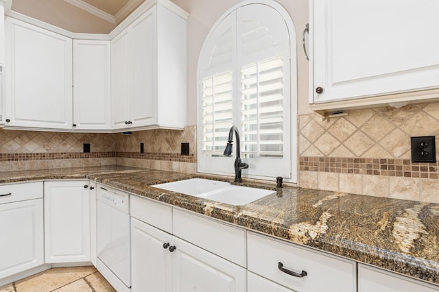 kitchen featuring white dishwasher, sink, white cabinetry, and dark stone countertops