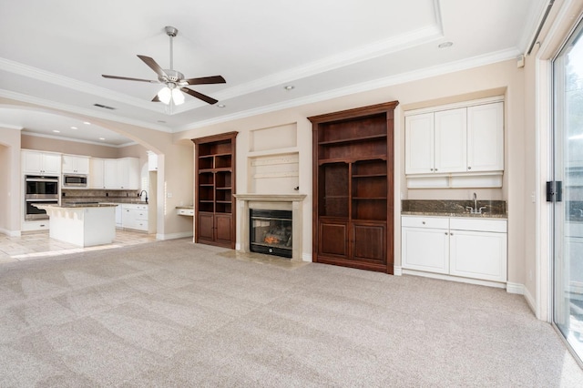 unfurnished living room featuring light carpet, ceiling fan, sink, and crown molding