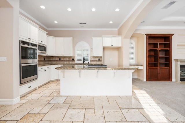 kitchen with stone counters, appliances with stainless steel finishes, an island with sink, a breakfast bar area, and white cabinets