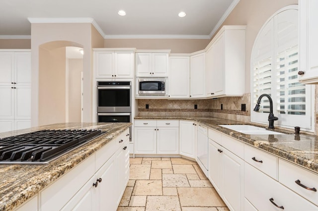 kitchen with appliances with stainless steel finishes, stone counters, crown molding, white cabinets, and sink