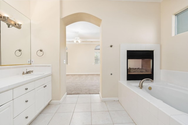 bathroom featuring ceiling fan, vanity, tiled bath, tile patterned floors, and a multi sided fireplace