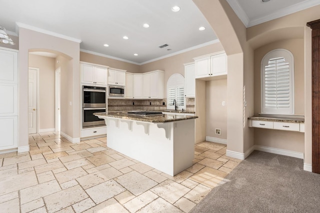 kitchen featuring stainless steel appliances, a kitchen bar, white cabinets, and dark stone counters